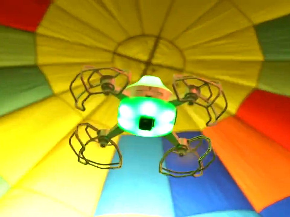 Close-up of an indoor show drone in flight, its LED body lit green inside protective propeller guards